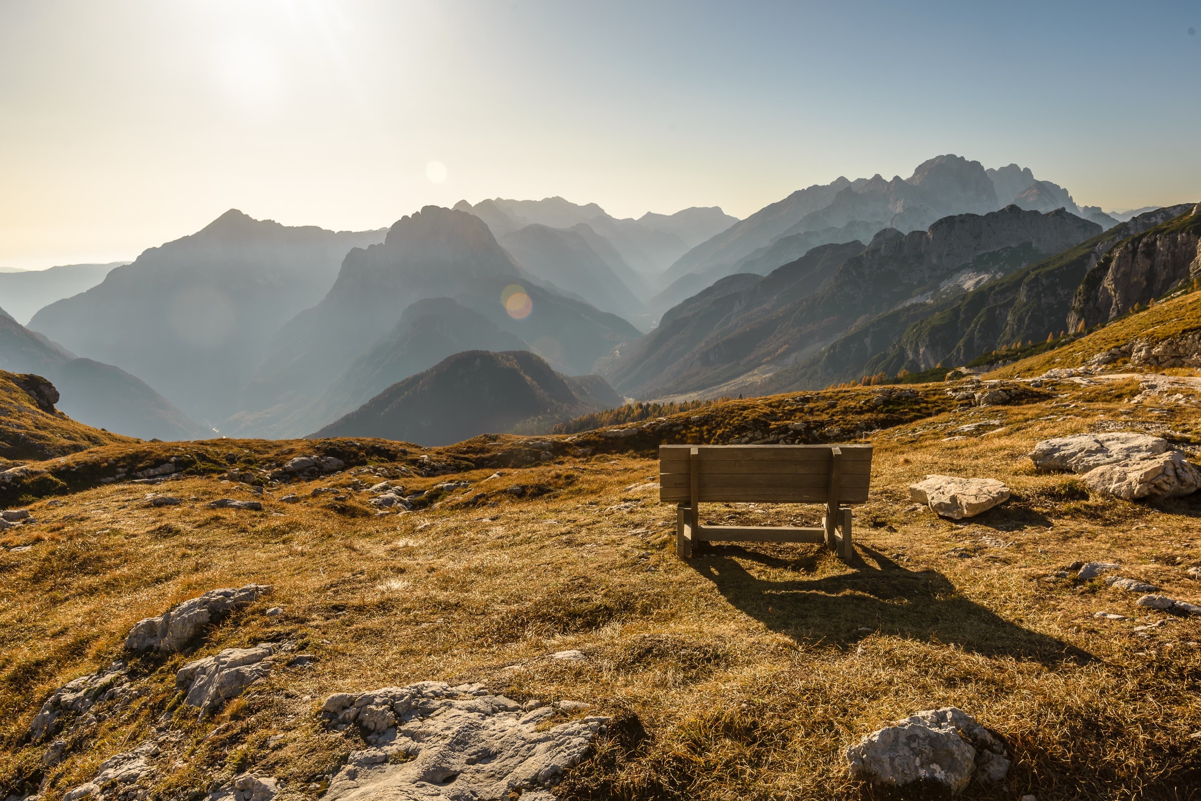 Empty wooden bench on a golden alpine meadow overlooking layered mountains at sunset